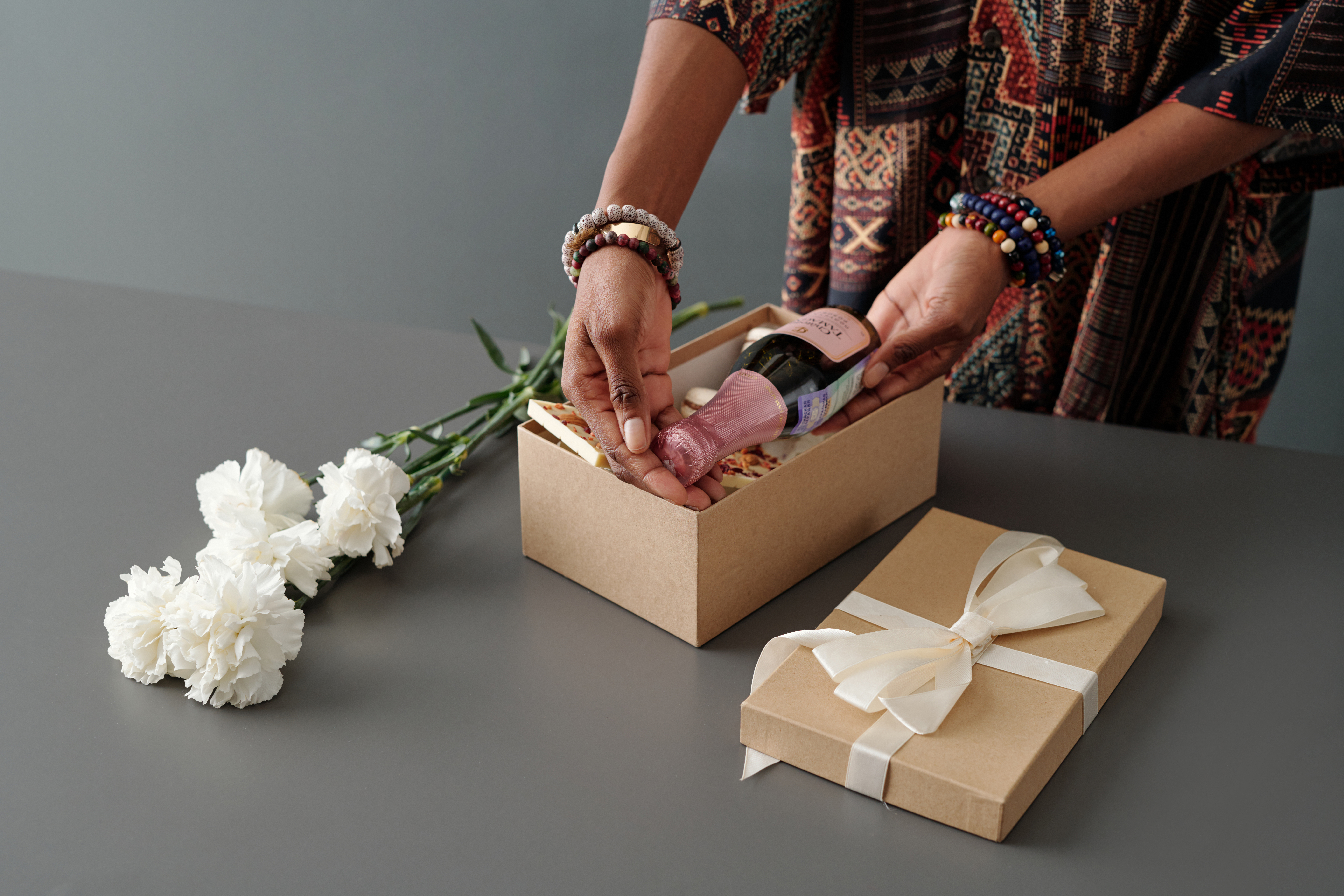 Hands of young unrecognizable African American woman putting small bottle of champagne into giftbox with present